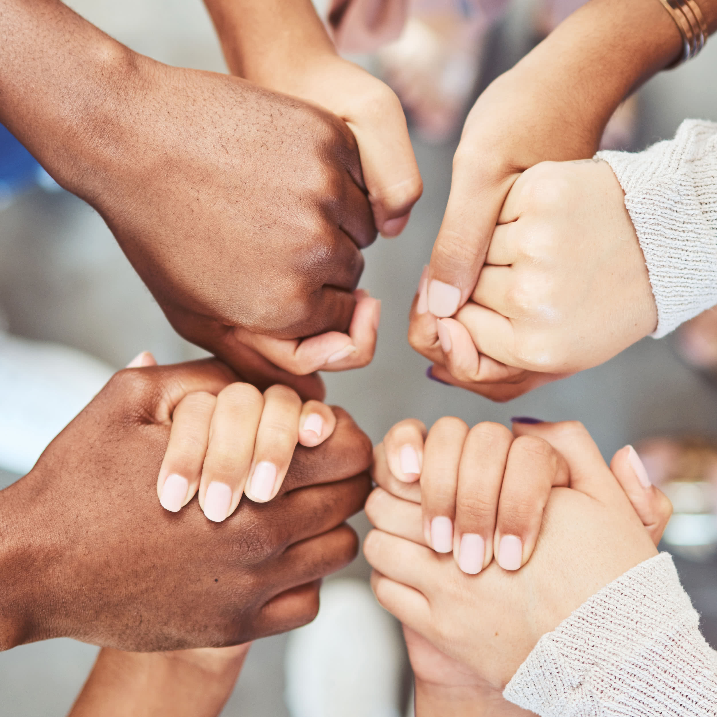 Close-up of hands; a diverse group of people holding hands in a circle