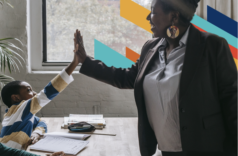 A woman high-fives a young boy who is working in a classroom.